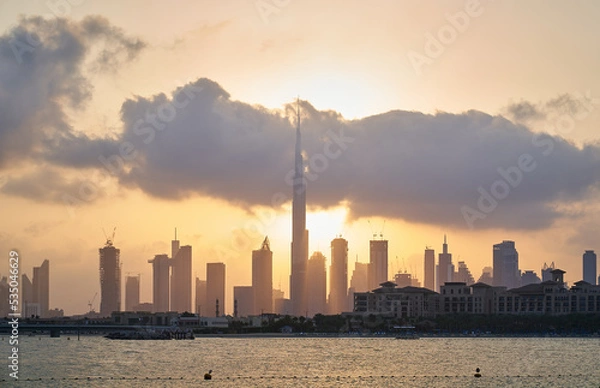 Fototapeta sun coming out from behind clouds and Dubai skyline