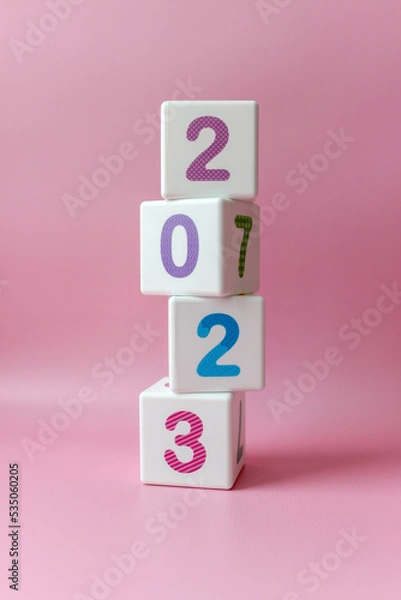 Fototapeta Cube tower with colorful numbers 2023 in center of the photo on pink background. New year, calendar.