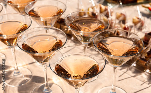 Fototapeta Sparkling wine is poured into glasses illuminated by the sun.