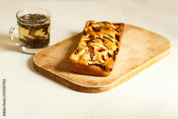 Fototapeta Autumn cake and a cup of tea. Autumn mood. Charlotte with apples and plums lies on a wooden board.