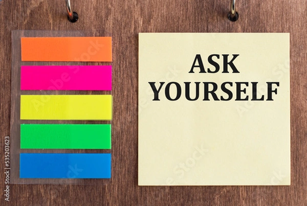Fototapeta The words ASK YOURSELF written in a yellow card on a wooden background near multi-colored markers