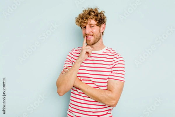 Fototapeta Young caucasian man isolated on blue background smiling happy and confident, touching chin with hand.