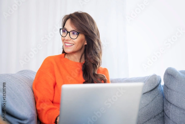 Fototapeta Smiling woman using her laptop and working at home