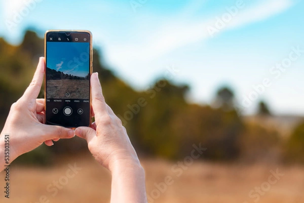 Fototapeta Woman's hands taking a photograph of the landscape with a smartphone.