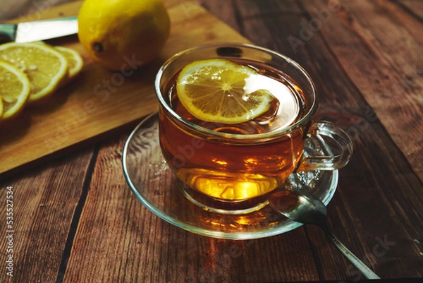 Fototapeta transparent mug with black tea and yellow lemon on the table.