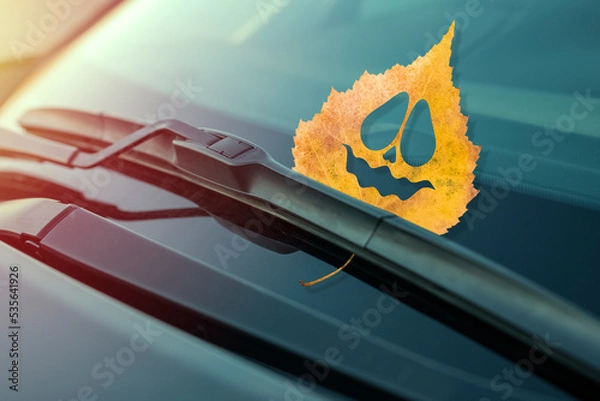 Fototapeta Autumn leaf with cheerful emotion, on the windshield of the car under the brush. Concept of warm autumn or Halloween holiday. Close-up