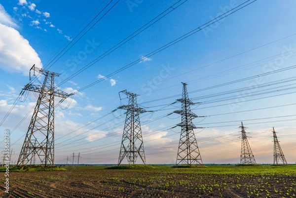 Obraz high voltage lines and power pylons in a green agricultural field against a saturated sky