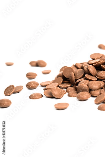 Fototapeta Close up of milk chocolate chips. Scattered chocolate callets isolated on white. Texture of chocolate. Vertical photo