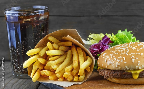 Fototapeta French fries in a paper with hamburger, green salad and glass full of cola