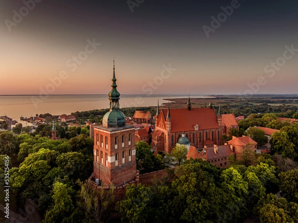 Fototapeta Great view of the beautiful city of Frombork located in Warmia, Poland. Cathedral Hill among trees at sunset.