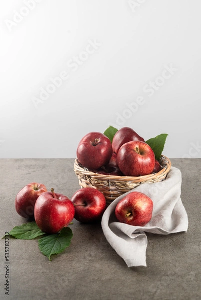 Obraz Ripe apples in basket on stone table with gray napkin, front view, white background, copy space
