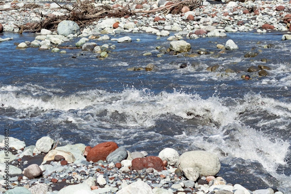 Fototapeta White water of the  mountain stream in summer time. Torrent waves, white and brown stones, green grass on the bank