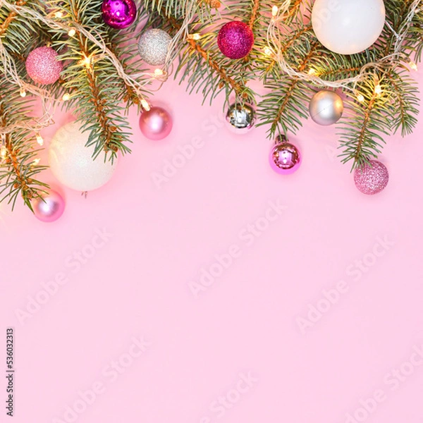 Fototapeta Pastel pink background with copy space and silver pine branches decorated with pink and white ornaments and lights. Flat lay