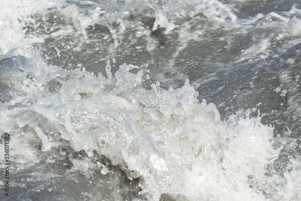 Fototapeta Close-up white water of the mountain stream in a summer day. White and grey foam of waves and drops of water