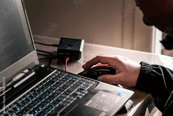 Fototapeta Close up of man's hand using wireless mouse and laptop computer with blue backlit keyboard