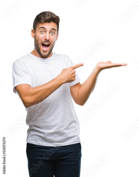 Fototapeta Young handsome man over isolated background amazed and smiling to the camera while presenting with hand and pointing with finger.