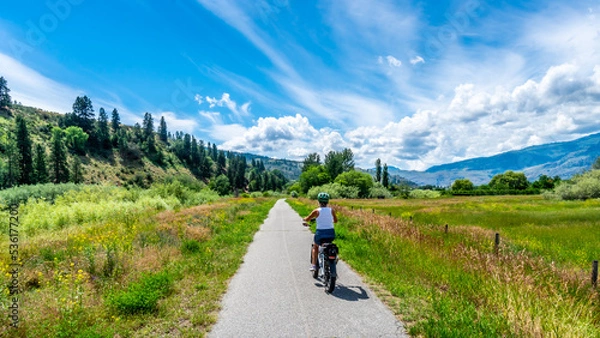 Obraz Woman on an e-bike on the trail along the Okangen River Canal between Oliver and Osoyoos in the Okanagen Valley of British Columbia,  Canada