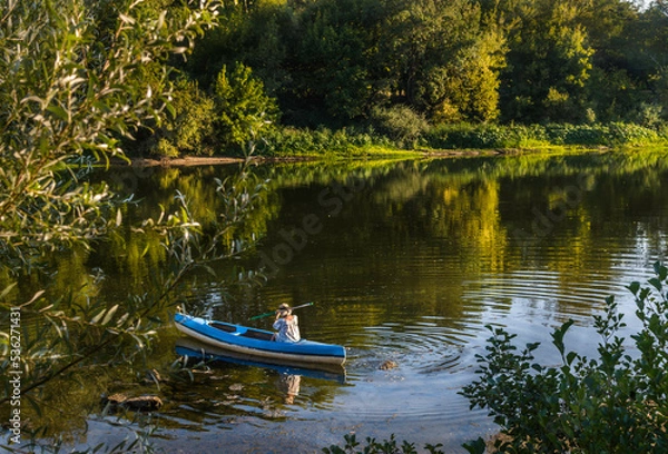 Fototapeta woman kayaking in a boat in a calm river. Beautiful lanscape. Concept of relaxation, wellbeing, tranquility, enjoyment in nature. 
