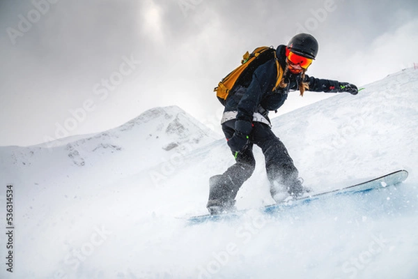 Fototapeta snowboarder quickly descends creating a wave of snow against the backdrop of mountains. ski resort. off-piste, free-riding
