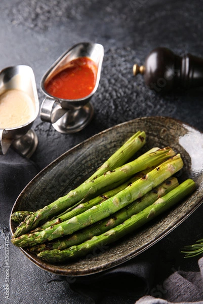 Fototapeta Grilled vegetables. Fried asparagus with herbs on a plate, red and white sauces, ketchup, spices. Rosemary on a dark table. Turkish cuisine, dish. Vegetable garnish. Background image, copy space
