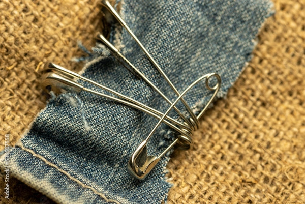 Fototapeta Safety pins on a strip of denim against a homespun fabric with a rough texture.