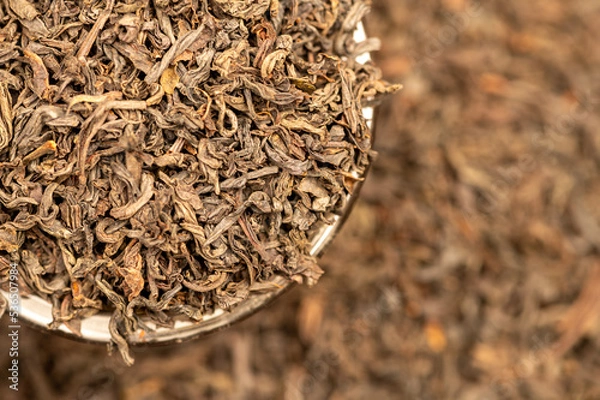 Fototapeta Large-leaf black tea in a glass and scattered on the table. Close-up of the surface texture