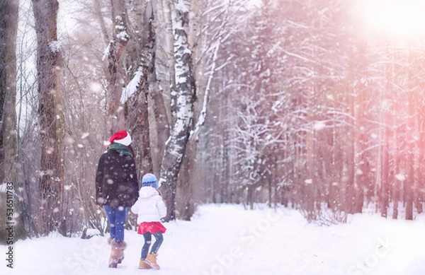 Fototapeta A winter fairy tale, a young mother and her daughter ride a sled in the forest. A girl on a sled with gifts on the eve of the new year in the park. 