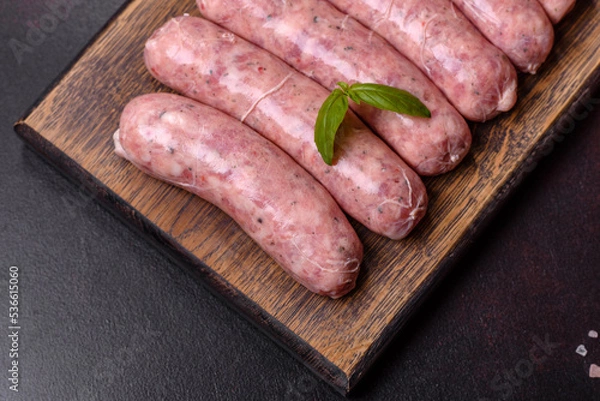 Fototapeta Raw sausages with ingredients on a cutting board on a dark concrete background with copy space