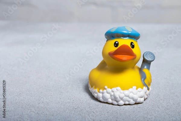Fototapeta Yellow rubber duck for a bath in a bath cap and with a shower head in the wing on a light background