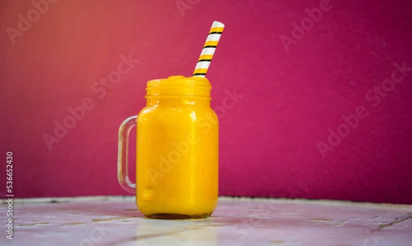 Obraz Mango smoothee with straw on a wooden table on pink background