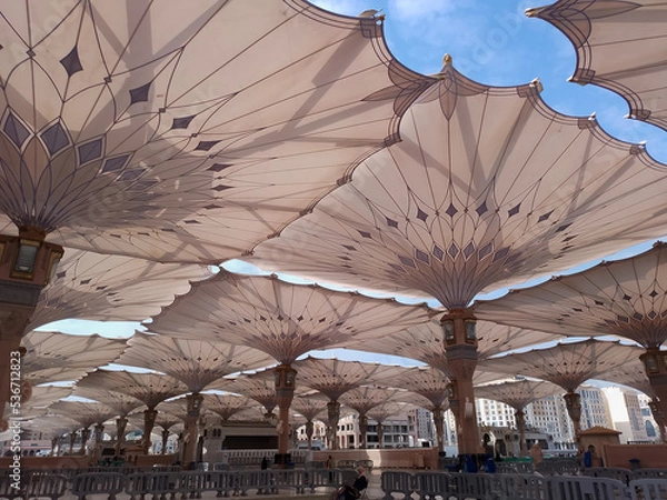 Obraz Medina, Saudi Arabia - October 07, 2022: Umbrella construction on the square of Al-Masjid An-Nabawi or Prophet Muhammed Mosque are protecting people from sun at daytime and work as lights at night