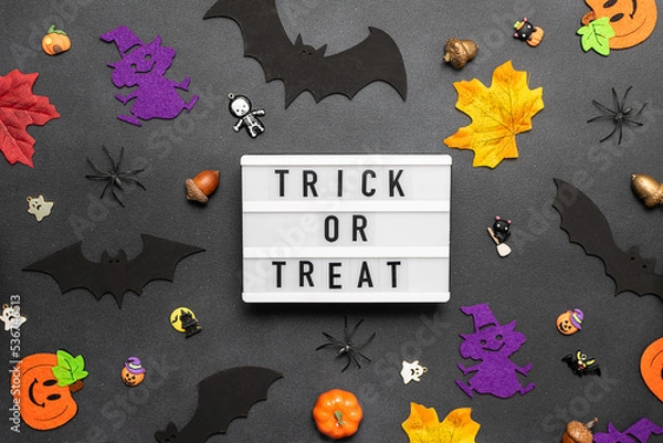 Fototapeta Lightbox with text Trick or Treat on black stone background decorated with traditional Halloween symbols such as bats, pumpkinns and spiders. 