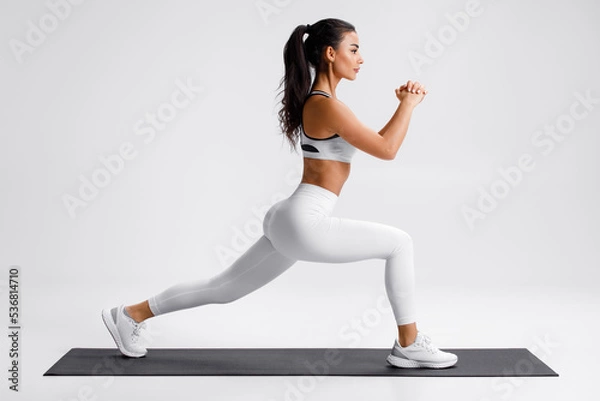 Fototapeta Fitness woman doing lunges exercises for leg muscle training. Active girl doing front forward one leg step lunge exercise