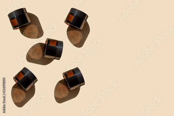 Obraz Mockups of glass jars, amber in color, with moisturizer, arranged in chaotic manner on beige background. Containers with cosmetics cast hard shadow on surface. Close-up, copy space, flat lay
