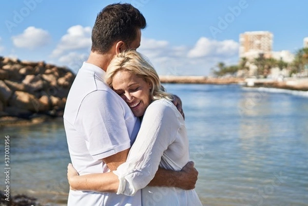 Fototapeta Middle age man and woman couple hugging each other standing at seaside