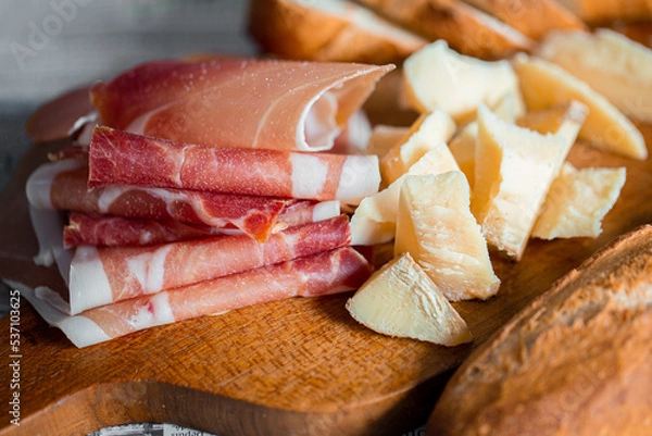 Obraz Wooden board with cheese and ham. Board with jamon and cheese. Aperitif on the board. Jamon with bruschetta and parmesan.Delicious appetizer for wine.Italian appetizer. Jamon and salami with cheese.