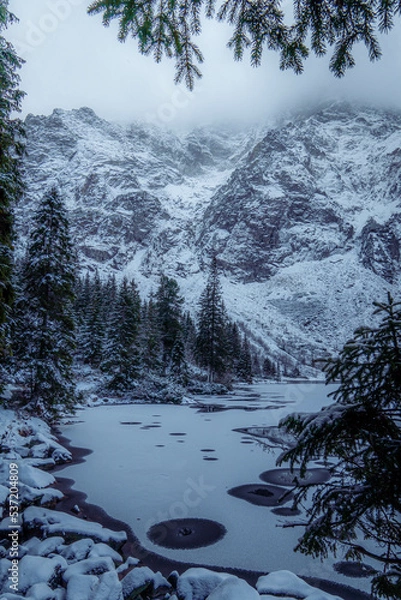 Obraz Moody winter photo of a frozen lake surrounded by high mountains and pine trees