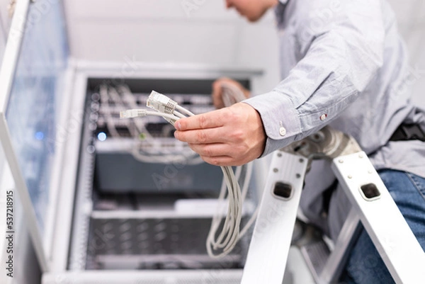 Fototapeta Male technician's hand holds group of white network cables before connecting to port switch.