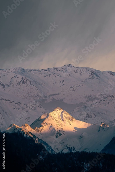 Obraz Peak of a mountain lit by the settling sun surrounded by a range of mountains