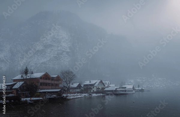 Obraz Typical alpine style buildings in the distance over the lake in Hallstatt, Austria during a snowy winter afternoon.