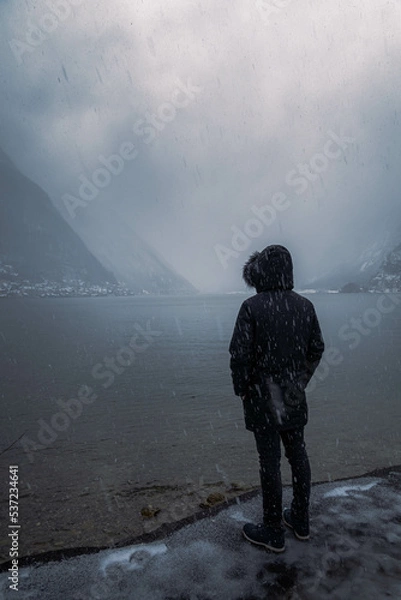 Obraz Melancholic photo of a young man staring at the distant alpine village during a cold winter afternoon