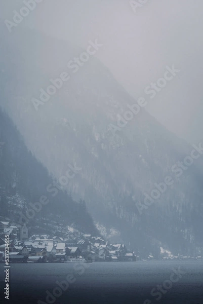 Obraz Typical alpine style buildings in the distance over the lake in Hallstatt, Austria during a snowy winter afternoon.