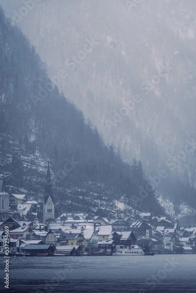Obraz Typical alpine style buildings in the distance over the lake in Hallstatt, Austria during a snowy winter afternoon.