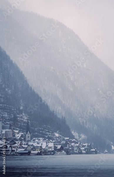 Obraz Typical alpine style buildings in the distance over the lake in Hallstatt, Austria during a snowy winter afternoon.