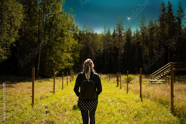 Fototapeta walk of a light-haired woman dressed in black with a backpack in the bosom of nature - a landscape park in Finland