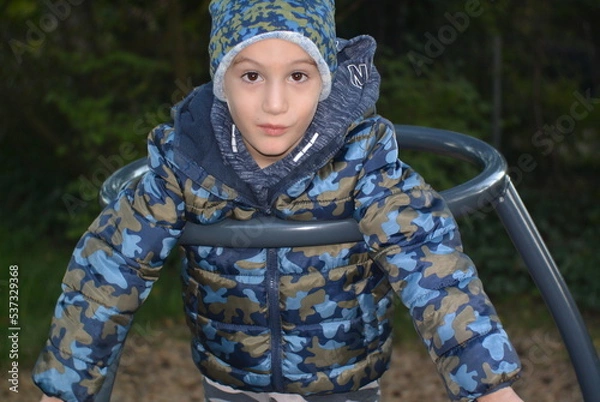 Fototapeta portrait of a child on a playground (merry go round) in a camouflage jacket 