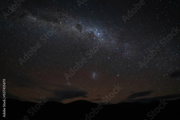 Fototapeta Silhouette of mountains with the beautiful Milky Way above, in the background you can see a dark starry sky with some faint clouds, constellations and stars shining bright.