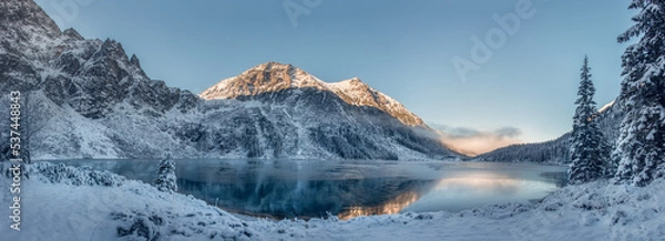 Fototapeta Amazing beautiful scenic of Tatra mountains and Eye of the Sea lake, Poland. Bright sunrise above mountains in winter. Fir woods covered snow. The lake is not covered with ice.  