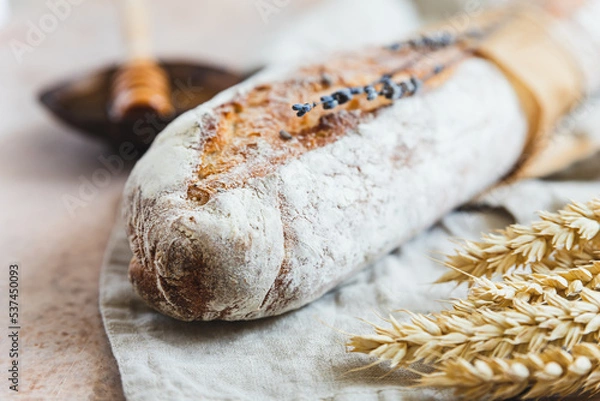 Fototapeta Loaf of artisan sourdough bread with lavender and honey on linen napkin with wheat ears, concrete background. Traditional artisan bread.
