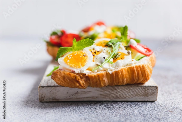 Obraz Variety of croissant sandwiches with tomato, cucumber, mozzarella cheese, eggs and mashed avocado with mint and arugula. Open savory sandwiches. Tasty healthy breakfast.